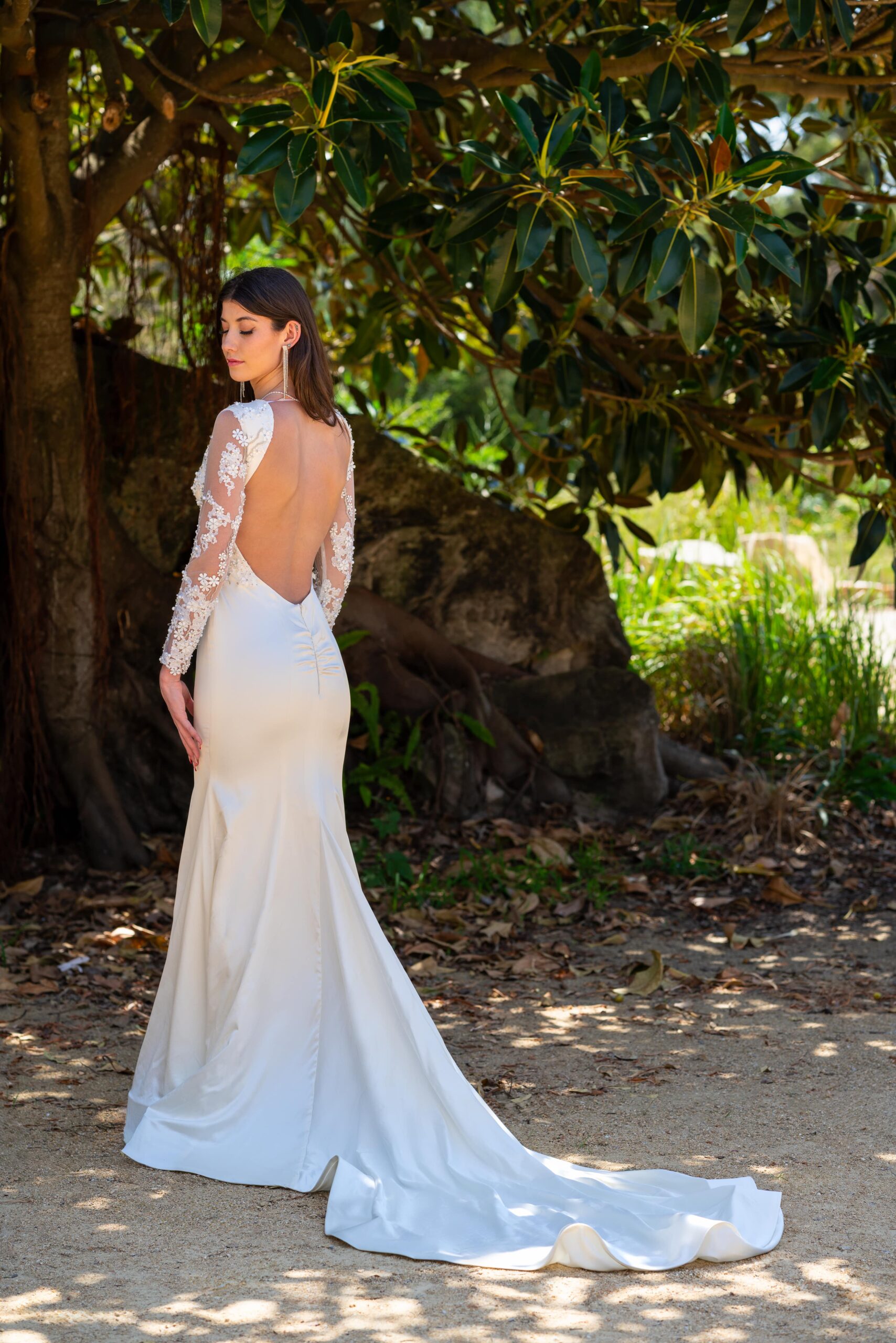 Woman posing in a stunning sleeved wedding dress showing off the open back